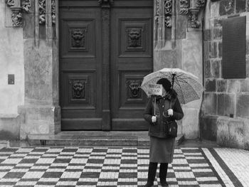 Woman holding umbrella and sign while standing against building