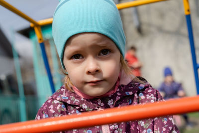 Worried preschooler looking at camera with serious expression while standing near house on street. 