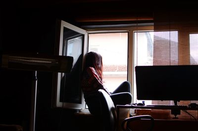 Side view of woman sitting on window sill at home