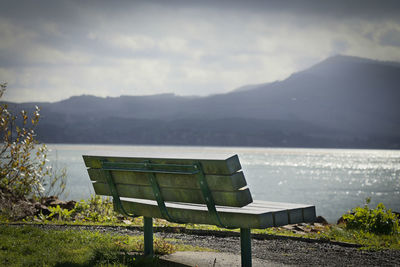Empty bench by lake against mountains