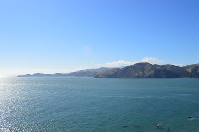 Scenic view of sea and mountains against clear blue sky