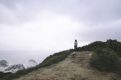 Rear view of hiker standing on trail against sky