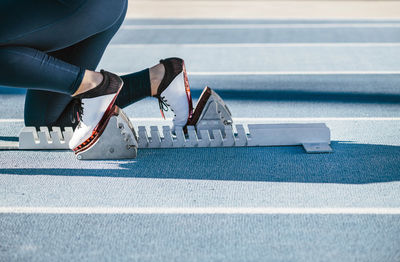 Unrecognizable cropped sportswoman in sportswear beginning race from crouch start position on starting blocks in a sunny day on stadium