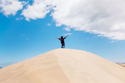 Man with arms outstretched standing on sand
