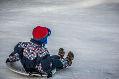 Rear view of boy tobogganing on snow covered field during winter