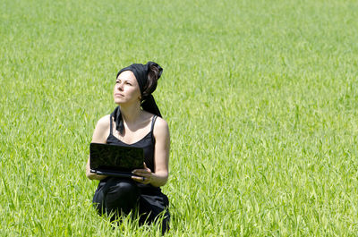 Mature woman holding laptop while sitting on grassy field