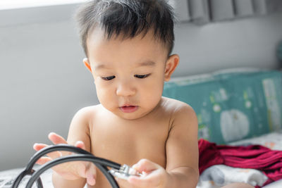 Portrait of cute baby boy holding stethoscope while sitting on bed at home