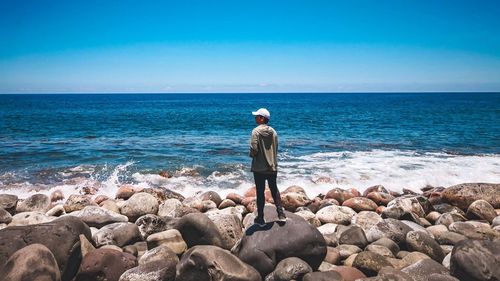 Full length of man standing on rock at beach against sky