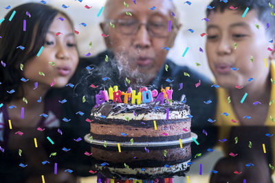 Grandparents and grandchildren blowing birthday candles on cake at home