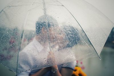 Close-up of couple seen through wet umbrella