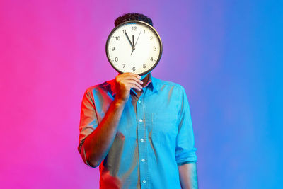 Man holding clock in front of face against colored background