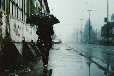 Rear view of woman with umbrella walking on road during rainy season