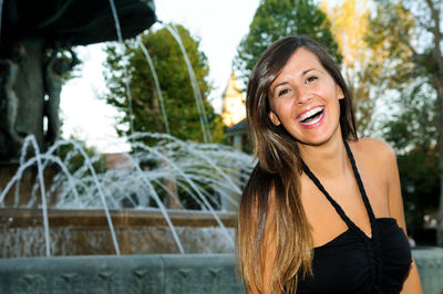 Portrait of happy young woman standing against fountain