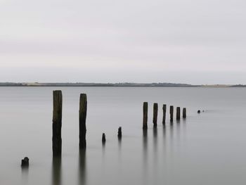 Wooden posts in lake against sky