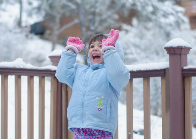 Cute girl with mouth open standing by railing during winter