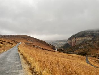 Empty road leading towards mountains against sky