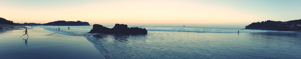 Silhouette rocks on beach against sky during sunset