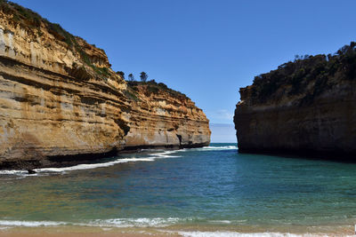 Rock formations on beach against clear blue sky