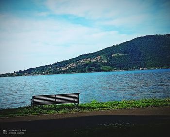 Empty bench by lake against sky