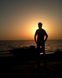 Silhouette man standing at beach against sky during sunset