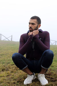 Young man sitting on field against clear sky