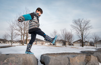 Young boy taking a big step across large rocks on a winter day.