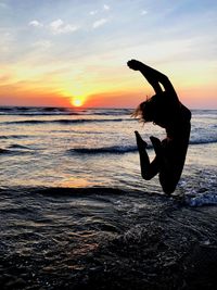 Silhouette woman jumping on beach against sky during sunset