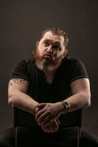 Portrait of man sitting against black background