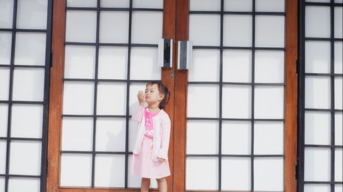 Girl looking away while standing against window