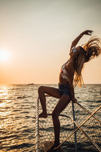 Woman standing by sea against sky during sunset