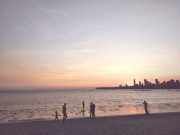 Silhouette people at beach against sky during sunset