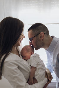 Dad kissing newborn baby boy. mom holding son. happy family of three