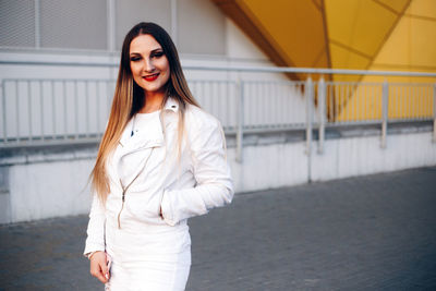 Portrait of smiling beautiful young woman standing against building