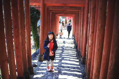 Full length of girl standing on footpath amidst wooden posts