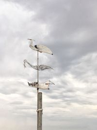 Low angle view of weather vane against cloudy sky