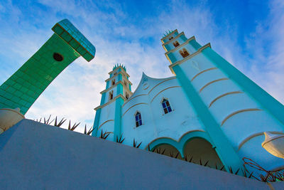 Low angle view of cross amidst buildings against blue sky