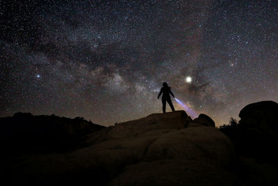 Silhouette man standing on rock against sky at night