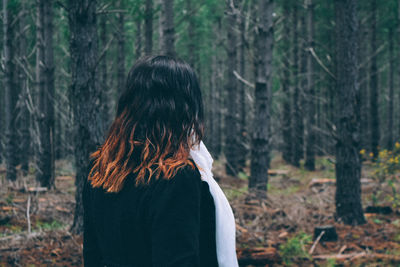 Rear view of woman standing amidst trees at forest