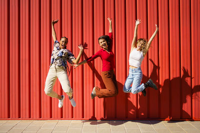 Cheerful female friends jumping against red wall