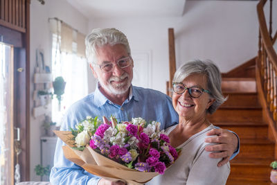 Portrait of smiling couple holding bouquet at home