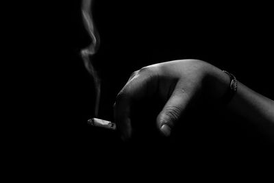 Close-up of hand holding cigarette against black background