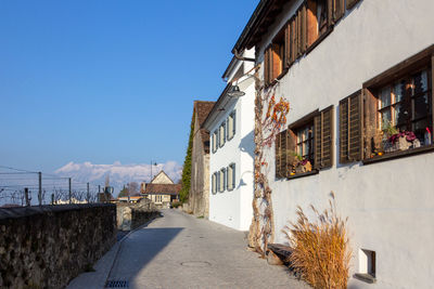 Footpath amidst buildings against blue sky