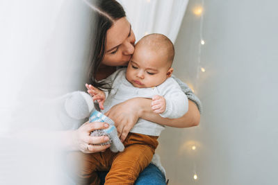 Young mother playing with cute baby boy in the bright bedroom, natural tones, love emotion