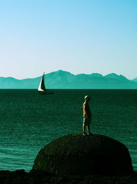 Man standing on rock formation in sea against clear sky