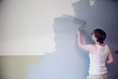 Rear view of woman painting wall in living room at home