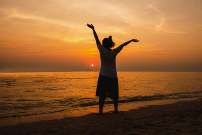 Rear view of man standing at beach during sunset