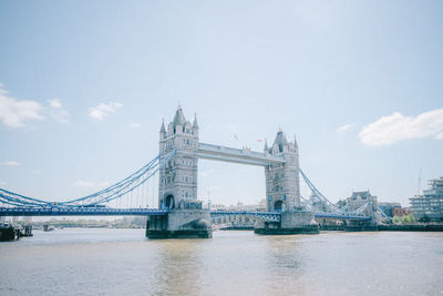 Bridge over river in city against cloudy sky