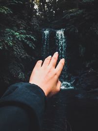 Cropped hand of woman gesturing against waterfall in forest