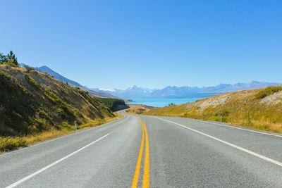 Empty road along landscape against clear blue sky