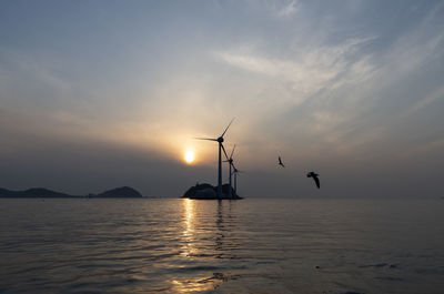 Silhouette sailboat in sea against sky during sunset